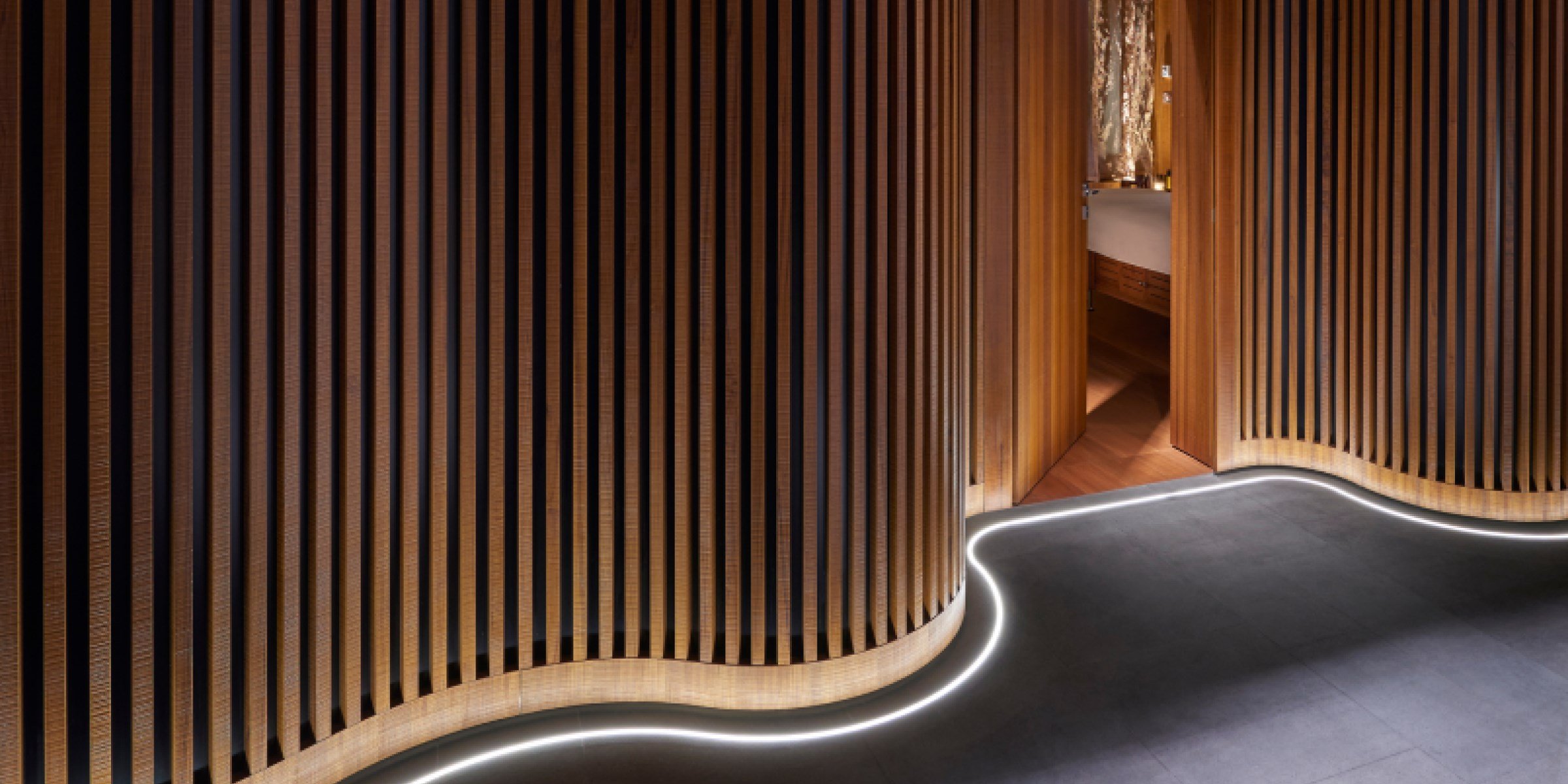 Modern interior with curved wooden slat walls and illuminated floor outlining an open door.