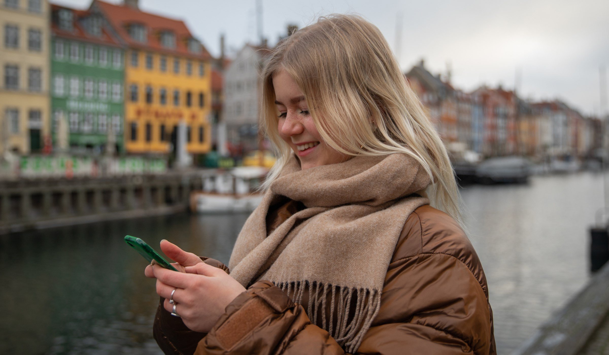 "Smiling woman using a smartphone by a colorful canal in Copenhagen