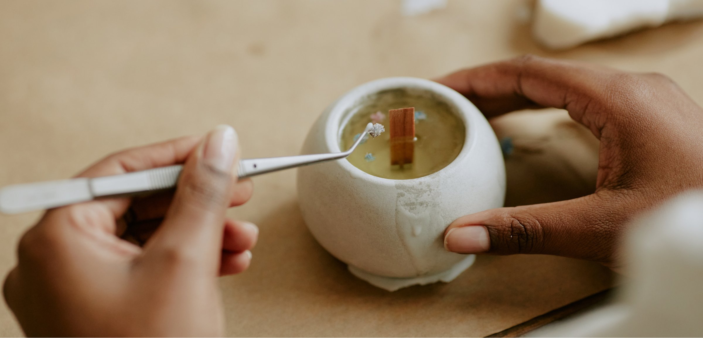 A close-up image of hands carefully placing a small decorative element into a candle that is in the process of being made. 