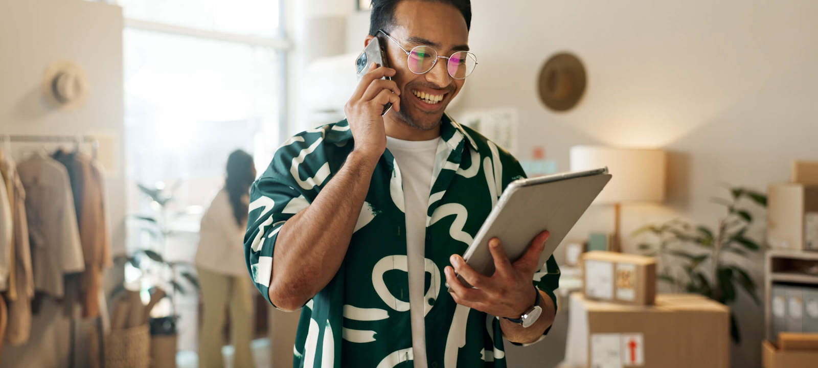 Smiling professional managing online business operations using a tablet and phone in a modern workspace.