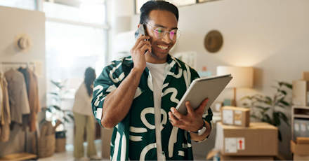 Smiling professional managing online business operations using a tablet and phone in a modern workspace.