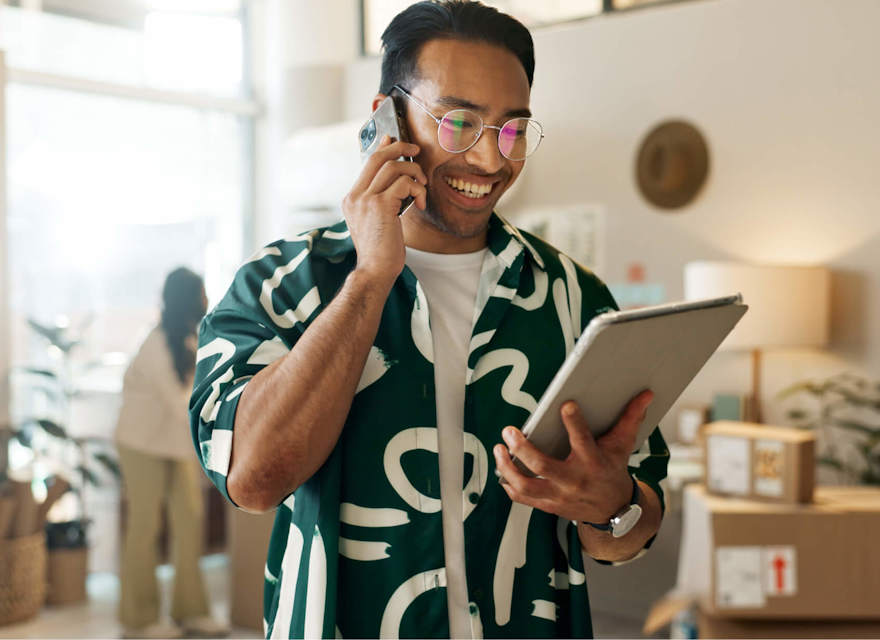 Smiling professional managing online business operations using a tablet and phone in a modern workspace.