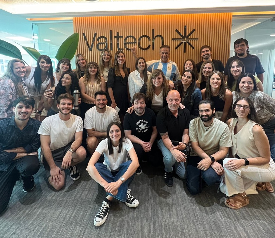 Large group of Valtech team members posing and smiling in front of company signage, highlighting collaboration, inclusivity, and vibrant workplace culture.