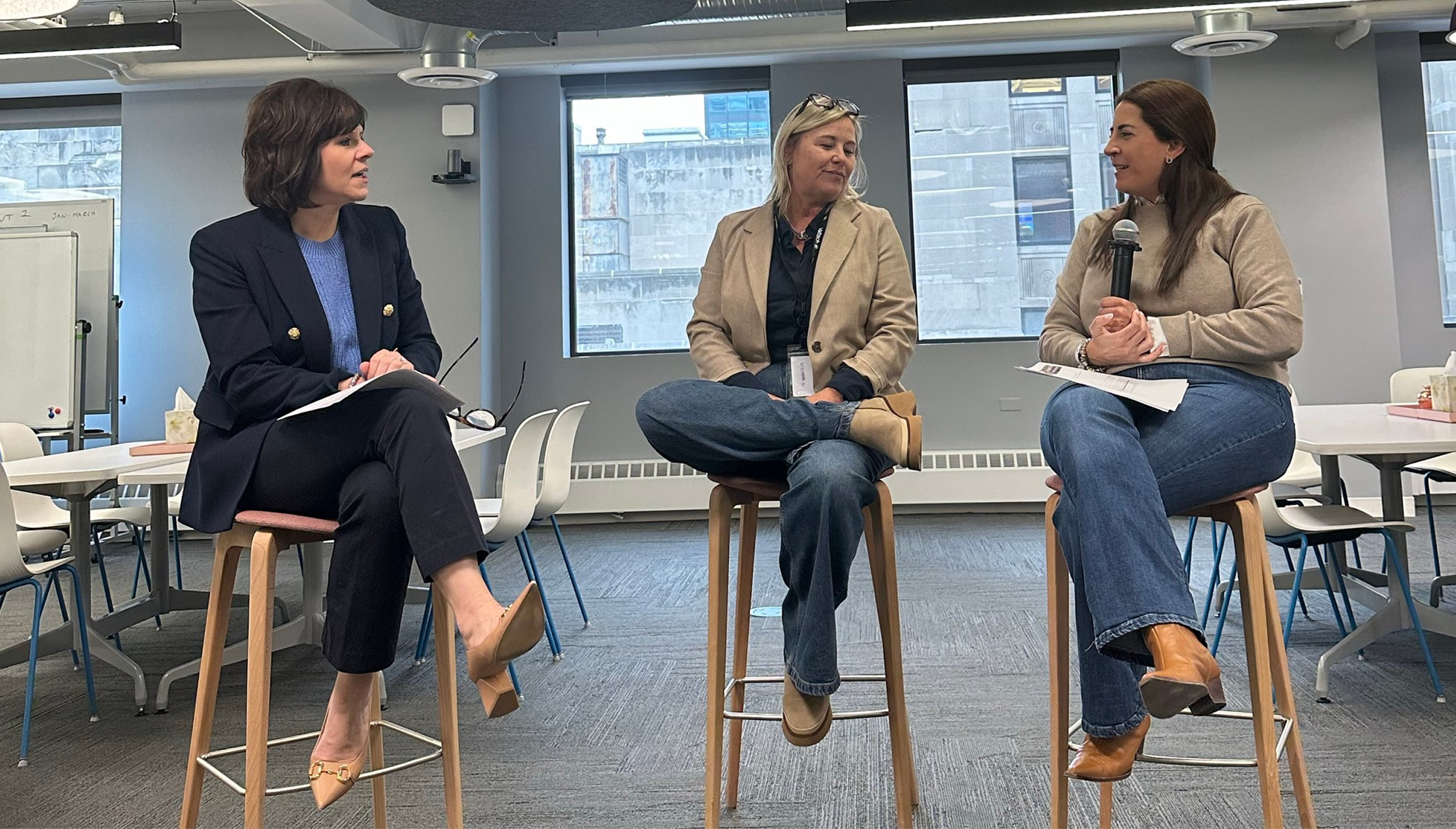 Three professional women engaged in a panel discussion in a modern office, highlighting leadership, collaboration, and workplace empowerment.