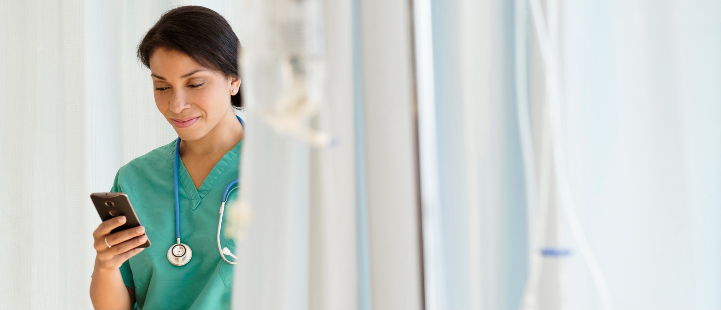 The image shows a doctor wearing a white coat and a stethoscope, looking intently at a smartphone in their hand. The focus is on the doctor's engagement with the phone, possibly reviewing patient data or using a healthcare app, reflecting the use of digital tools in medical practice.