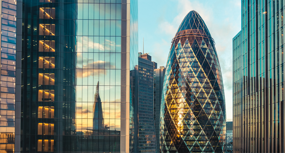 View of London’s modern financial district featuring The Gherkin and surrounding glass skyscrapers at sunset, symbolizing innovation and business hub.